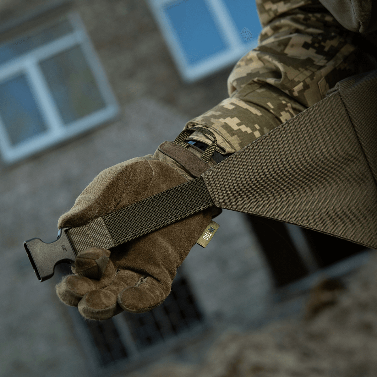 Person iført camouflagehandsker viser M-Tac Siddeunderlag med bælte for udendørs brug.