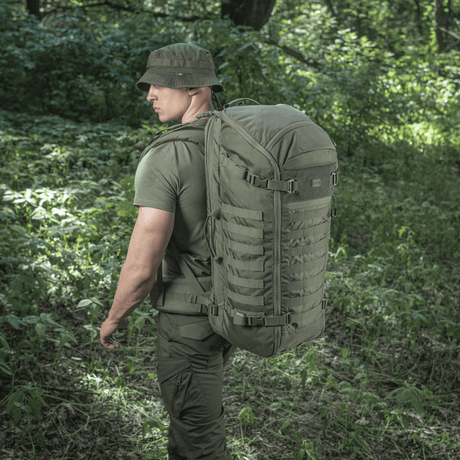 Mand bærer M-Tac Rygsæk Gen.II Elite Large i en skov. Rygsækken viser holdbar Cordura-materiale, ideel til udendørs eventyr.