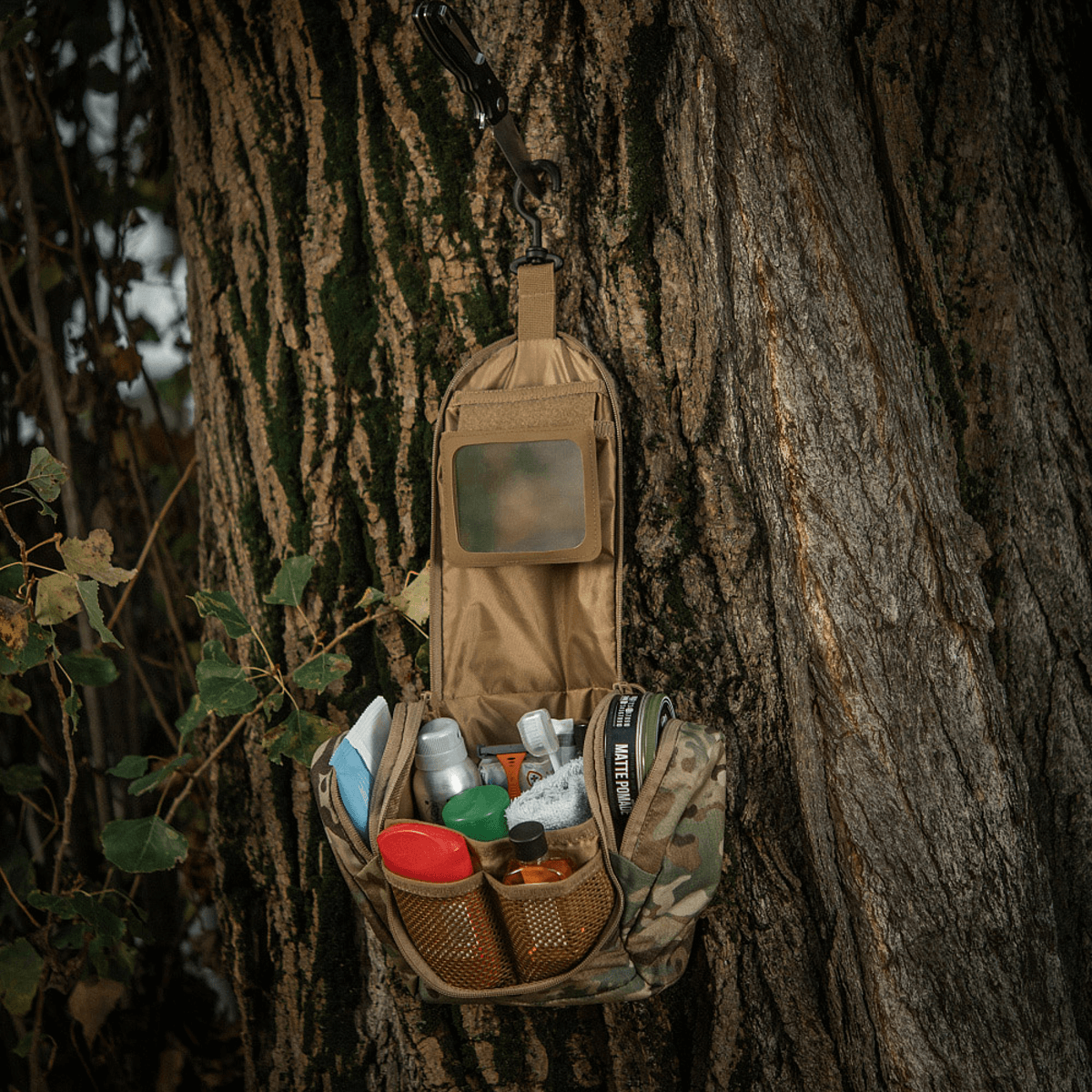 M-Tac Toilettaske Elite Gen.II hængende åben på et træ, fyldt med forskellige små hygiejneartikler til rejsebrug.