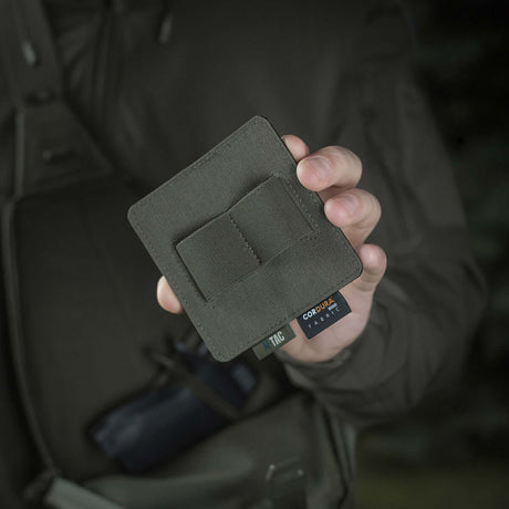 Henkilö pitelee M-Tac Double Mag Pouch Hook Backed Magazinea tumman taustan edessä