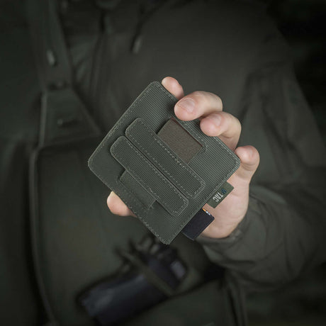 Henkilö pitelee M-Tac Double Mag Pouch Hook Backed Magazinea, sopii pistoolin lipuille ja multitoolille, kiinnitetty Velcrolla