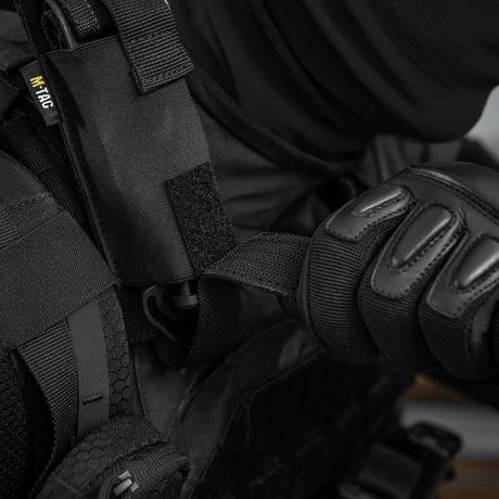 Henkilö pukeutuneena mustaan suojavarustukseen käyttää M-Tac Tourniquet Pouch Elastisk med MOLLE Gen.II:tä kiinnitettynä liiviin.