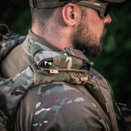 M-Tac Tourniquet Pouch Elastisk med MOLLE Gen.II taktiikkapukuisen miehen olkapäällä ulkona, nopea pääsy.