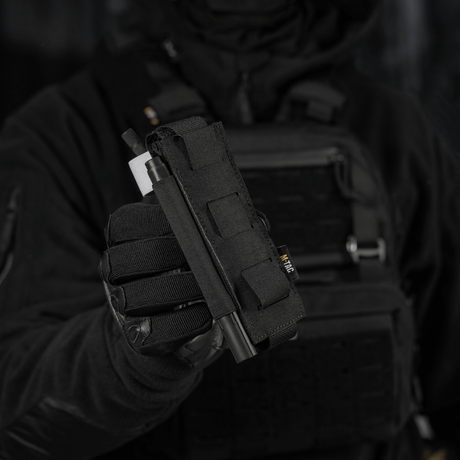 M-Tac Elastisk Tourniquet Pouch Molle Gen.III käytössä, pidetty henkilön toimesta taktisten varusteiden kanssa, korostaa toiminnallisuutta ja muotoilua.