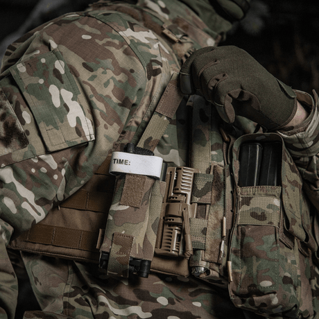 M-Tac Elastinen turnikekotelo Molle Gen.III kiinnitetty taktiseen liiviin tourniquetin ja lisävarusteiden kanssa sotilasalueella.