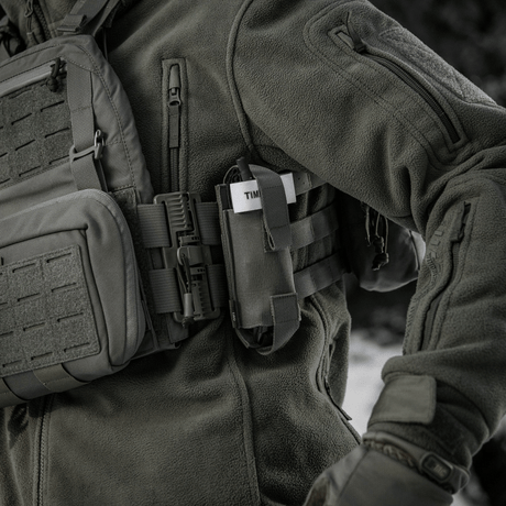 M-Tac Elastinen turnikekotelo Molle Gen.III kiinnitetty taktiseen takkiin henkilöllä kentällä.