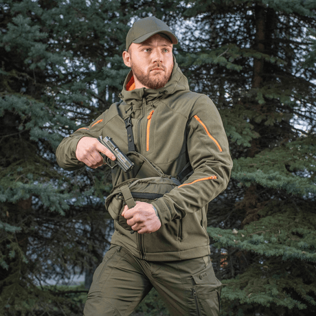 Mies kantaa M-Tac Sphaera Hex Hardsling Gen.II Elite -laukkua metsässä, valmis nopeaan toimintaan piilotetulla kantojärjestelmällä.