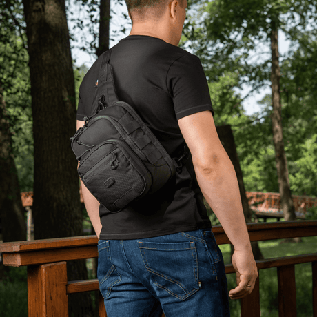 M‑Tac Cross Bag Elite Hex sling-laukku yhden olkapään kantoon, pidetään miehen toimesta mustassa t-paidassa, sopii päivittäis- ja taktiseen käyttöön