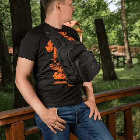 Mies kantaa M‑Tac Cross Bag Elite Hex sling-laukkua sillalla metsässä, sopii päivittäiseen käyttöön, laukku rymättää 5 litraa