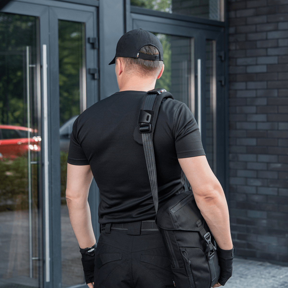 Mand med taske iført M‑Tac Skulderremspude 50 mm Elite ved indgangsdør.
