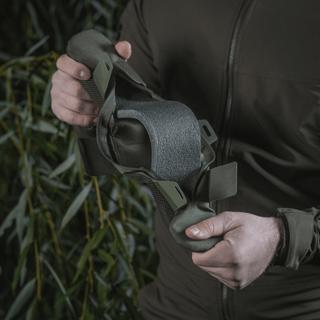 Henkilö pitelee M‑Tac olkahihnan pehmikettä 50 mm Elite, valmistettu kestävästä Cordurasta ja 3D-mesh mukavuuteen ja painonjakoon.