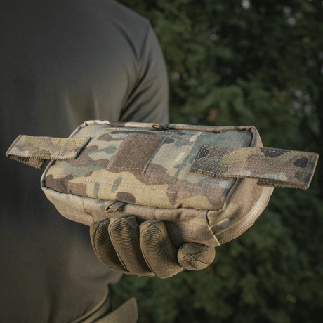 Henkilö pitää M‑Tac Horizontal Medical Pouch Eliteä maastokuvioisena, sopii kenttäkäyttöön ja ensiapuun, tukeva muotoilu ja vesitiivis vetoketju.