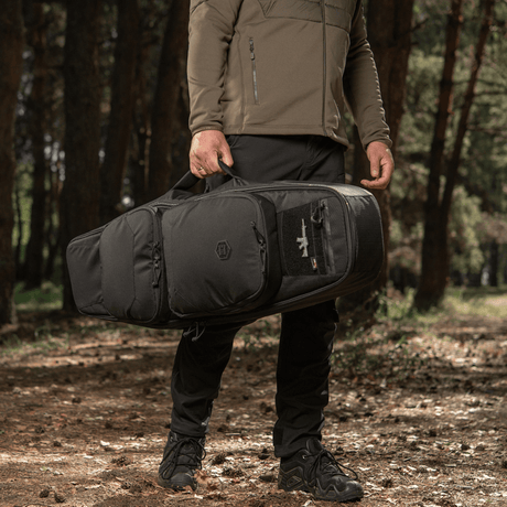 Mies kantaa M‑Tac Gun Backpack Case 105 cm Elite Hexiä metsässä, sopii metsästykseen ja ampumiseen, suunniteltu AR-15- ja AK-kivääreille.
