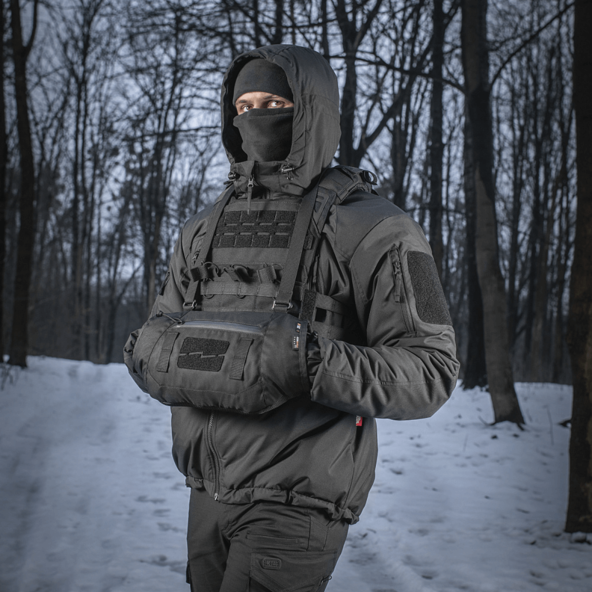 Person iført M-Tac Taktisk Håndvarmer Elite i skov med snebaggrund, holdende hænderne varme i det kolde vejr.