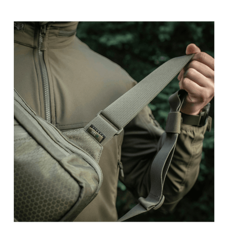 Mies kantaa M-Tac Sling Pistoltaske Elite Hexiä säädettävällä olkahihnalla Cordura-materiaalista.