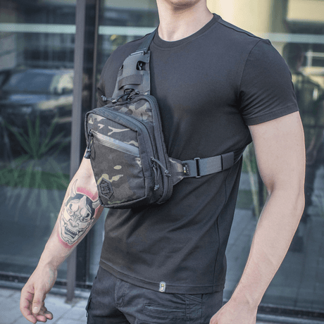 M-Tac Sling Pistoltaske Elite Hex miehen kantamana mustassa t-paidassa, näyttää laukun yksityiskohdat ja säädettävän olkahihnan.