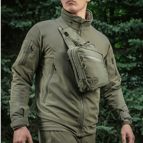 Mies, jolla on M-Tac Sling Pistoltaske Elite Hex, monipuolinen ja tyylikäs laukku piilotetulle aseelle, valmistettu Cordura 1000D -materiaalista.