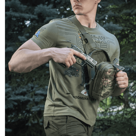 Mies kantaa M-Tac Sling Pistoltaske Elite Hexiä piilotetun aseen kanssa metsässä.
