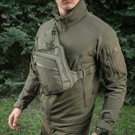 M-Tac Sling Pistoltaske Elite Hex Cordura-kankaasta, henkilön kantamana säädettävän hihnan kanssa metsätaustalla.