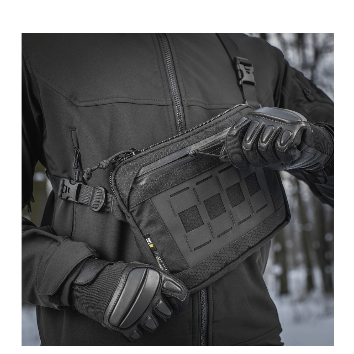 Person i sort jakke demonstrerer M-Tac Admin Taske Elite lavet af slidbestandigt Cordura materiale med lynlås og spænder i høj kvalitet.