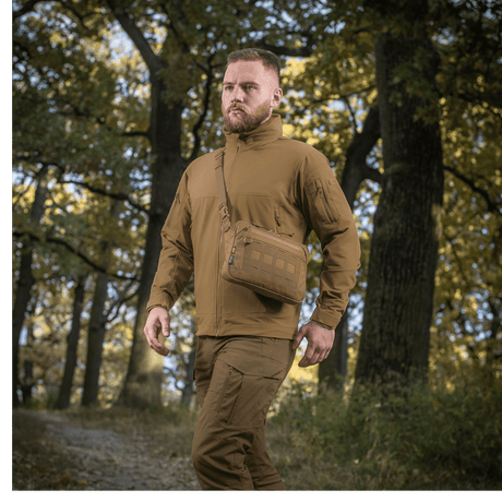 Mies metsässä M-Tac Admin-laukku Eliten kanssa, pukeutunut taktisiin vaatteisiin, säädettävä olkahihna, kestävä Cordura, luonnontausta