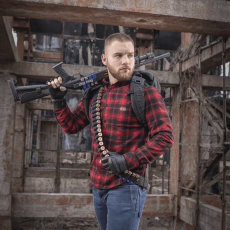 Mies kantaa M-Tac Bandolier Elitea ja ampuma-asetta teollisessa ympäristössä, suunniteltu nopeaan patruunoiden saatavuuteen.