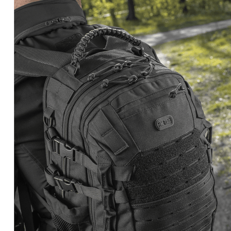 Mies käyttää M-Tac Mission Pack Elite -reppua ergonomisella muotoilulla ja MOLLE LASER CUT-systemillä metsäympäristössä.