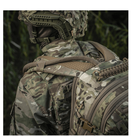 Henkilö camokuvioisessa asussa kantaa M-Tac Mission Pack Elitea MOLLE LASER CUT -järjestelmällä metsässä ergonomista toimivuutta varten.