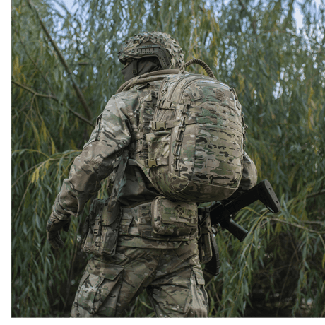 Sotilas kantaa M-Tac Mission Pack Elite -reppua camo-kuvioituna luonnossa.
