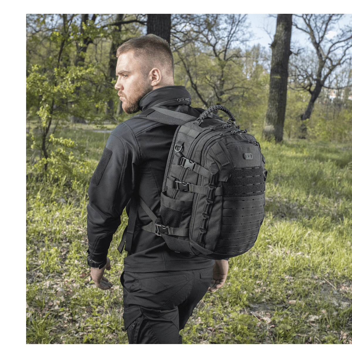 Mand bærer M-Tac Mission Pack Elite rygsæk i naturen, fremhæver det ergonomiske design og slidstærk Cordura 1000D materiale.