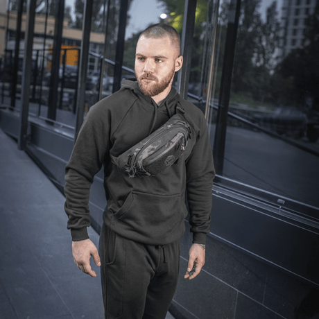 Mies pukeutuneena mustiin vaatteisiin kantaa M‑Tac Elite Hex -vyölaukkua ulkona. Kompakti ja tyylikäs laukku, sopiva arkeen ja taktiseen varustukseen.