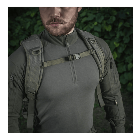 Mies pukeutuneena M-Tac Mission Rygsæk Elite Hex -reppuun, Cordura 1000D, ergonominen muotoilu ja MOLLE LASER CUT -järjestelmä metsäympäristössä.