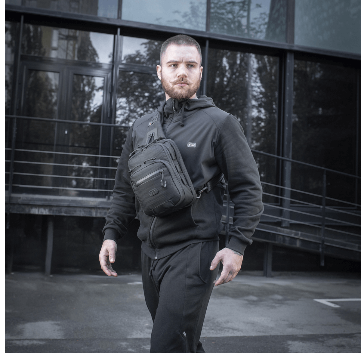 Mand med M-Tac Cross Taske Slim Elite Hex iført sort tøj foran moderne bygning