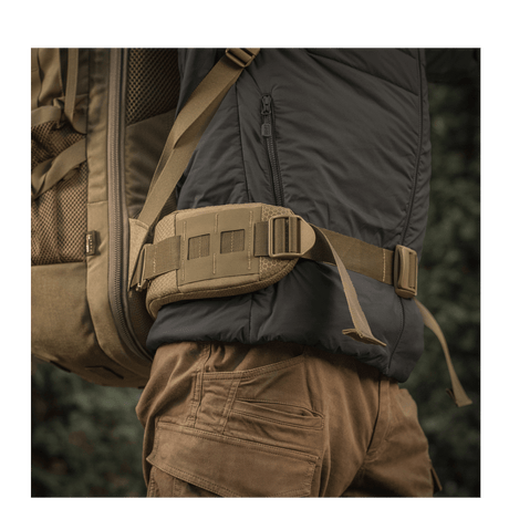 M-Tac reppu Large Elite Hex Gen. IV kantaa henkilö selässä ulkovaatteissa, sivulta luonnollisessa ympäristössä.