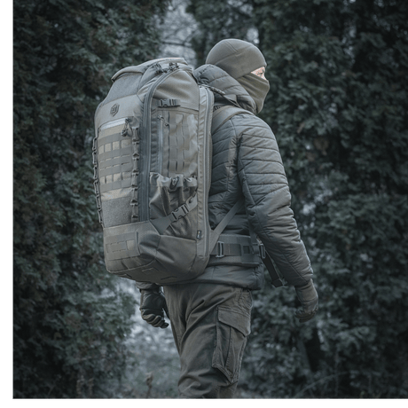 M-Tac reppu Large Elite Hex Gen. IV metsäympäristössä, suunniteltu aseiden kantamiseen ja suojaamiseen kestävästä Cordura-materiaalista.