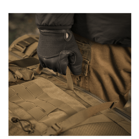 Käyttäjä hanskat kädessä pitää M-Tac reppu Large Elite Hex Gen. IV, tehty Cordura 500D- ja Hex 1000 -materiaaleista.