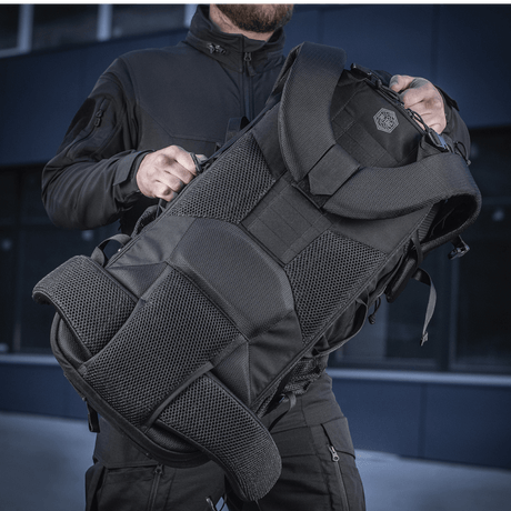 Henkilö pitää M-Tac Rygsæk Large Elite Hex Gen. IV -reppua ergonomisella muotoilulla ja kestävillä materiaaleilla, sopiva aseiden kuljetukseen.