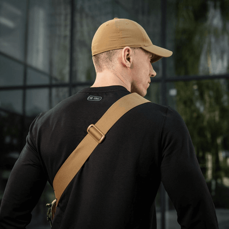 Mand iført sort trøje og beige kasket set bagfra med M-Tac Tablet Bag Laser Cut Hex skråt over skulderen.