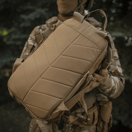 M-Tac STURM Elite Rygsæk holdt af en taktisk klædt person i naturen, fremstillet af Cordura for holdbarhed.