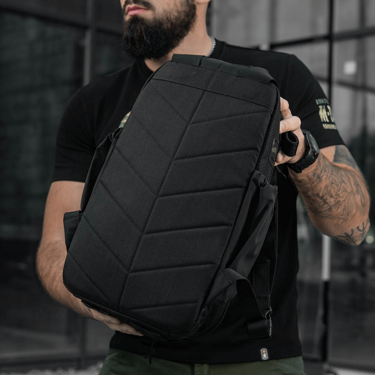 M-Tac STURM Elite Rygsæk holdt af model, udendørs præsenterende det taktiske design og holdbarhed, velegnet til kortvarige ophold i felten.