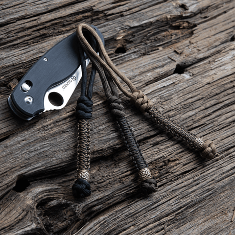 M-Tac Knife Lanyard Scandinavian tyylikäs punottu paracord taskuveitsille puupinnalla.