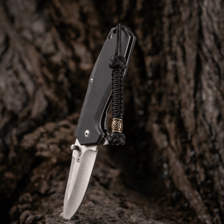 M-Tac Knife Lanyard Celtic, punottu paracord, asennettuna veitseen rustiikilla taustalla.