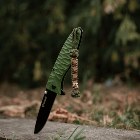 M-Tac Knife Lanyard Celtic - vihreä taittoveitsi punotulla paracord-lanyardilla ulkoilmassa.