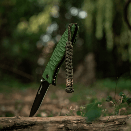 M-Tac Viper Lanyard Scandinavian punotulla paracordilla ja Viper-helmellä taskuveitsen vieressä luonnossa. Tyylikäs lisävaruste.