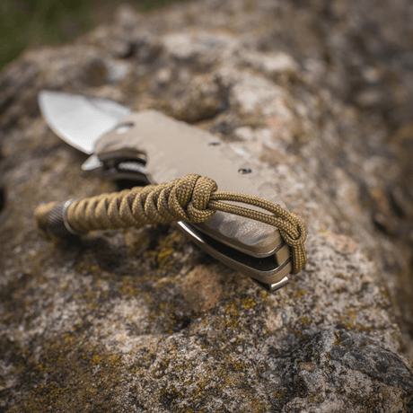 M-Tac Viper Lanyard Stainless Steel kiinnitettynä veitselle, esillä kivilaatalla. Joustava jatko-osa punotusta paracordista.