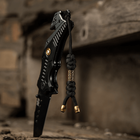 M-Tac Zeus Lanyard, punottu paracord kiinnitetty mustaan veitseen rustiikilla pinnalla, joustava lisä nopeaan käyttöön.