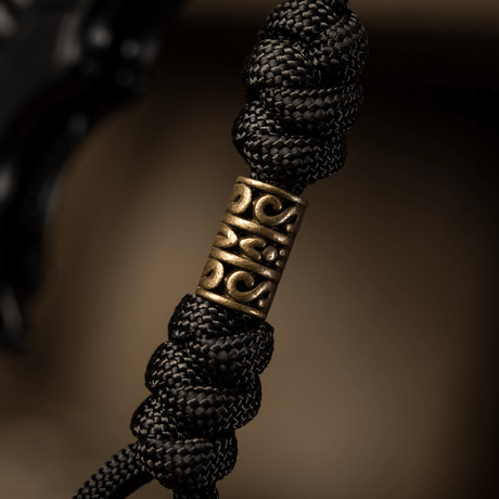 Yksityiskohtakuva M-Tac Zeus Lanyardista, punottu paracord ja koristeellinen messinkiosa, täydellinen veitselle ja varusteille.