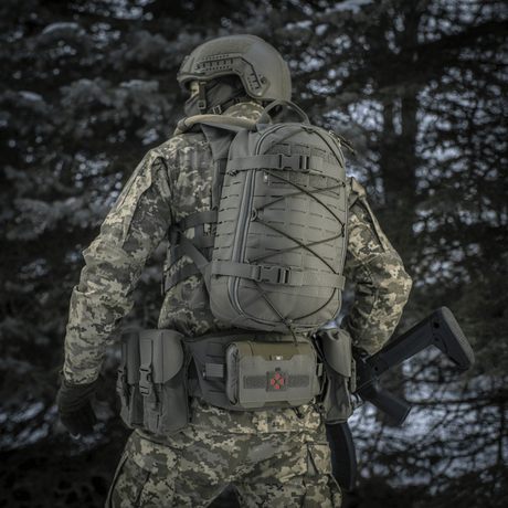 Taktinen henkilö M-Tac Sturm Elite Gen.II -repun kanssa metsäympäristössä, maastokuvioitu puku, nähty takaa.