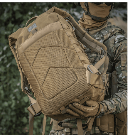 Sotilas M-Tac Large Assault Pack -repun kanssa urbaanissa maastokuviossa, näyttää MOLLE-kiinnityksen ja mukavat olkahihnat.