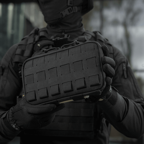 Henkilö pitelee M-Tac Admin Pouch Large Eliteä mustana, toimiva laukku taktisiin varusteisiin, Cordura 500D, tarrat ja laser-leikkaukset.